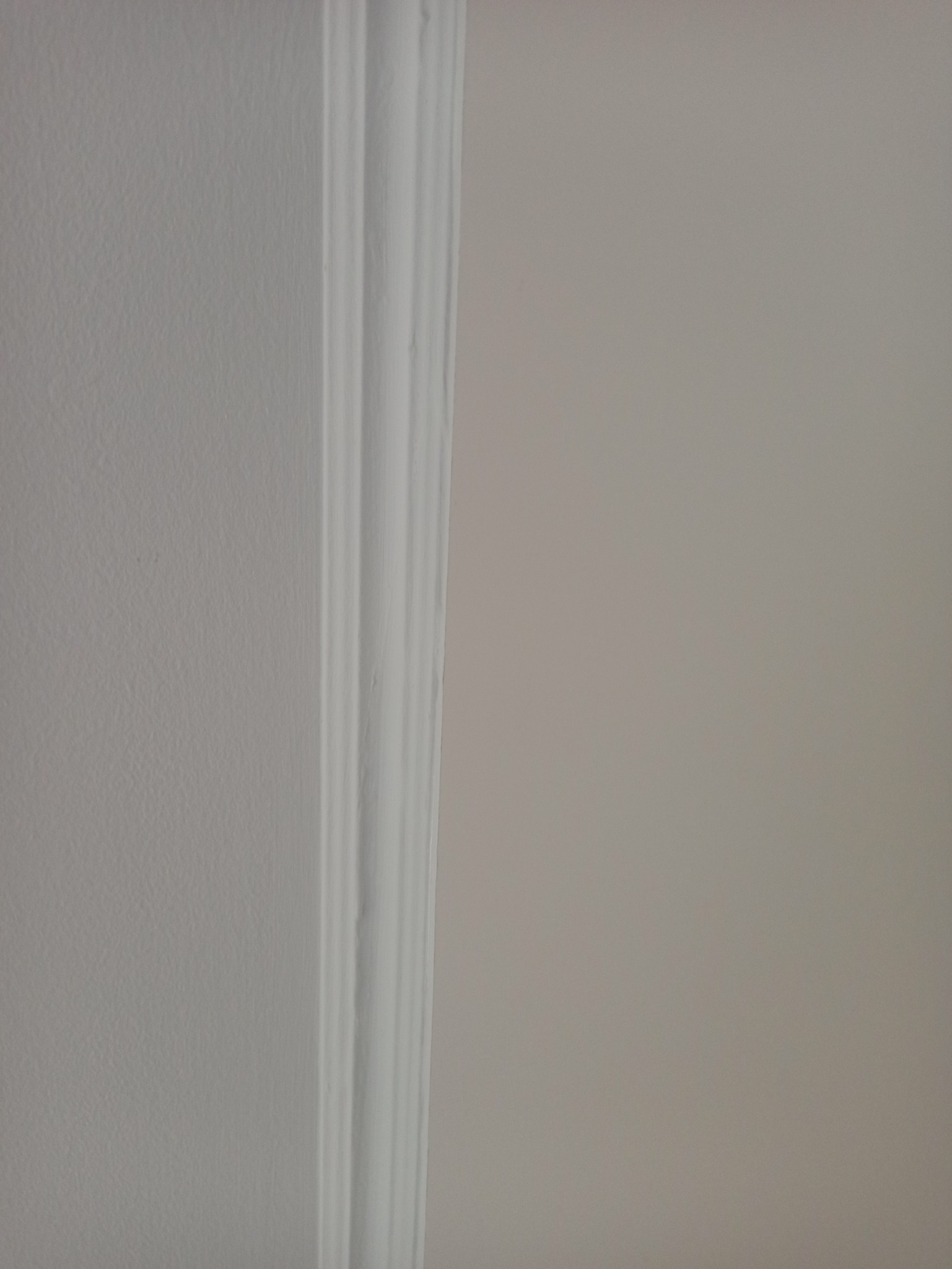 Fragment ściany z listwą dekoracyjną pomalowaną na biało, sąsiadującą z ścianą w odcieniu beżu.