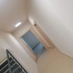 Klatka schodowa z jasnymi ścianami i podłogą, widok na otwarte drzwi do pomieszczenia w trakcie remontu.