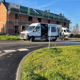 Dachy Kowalski Andrzej Kowalski - Budowa domu z częściowo wykonanym dachem, widoczni dekarze na dachu, na pierwszym planie samochód dostawczy z reklamą firmy dekarskiej.