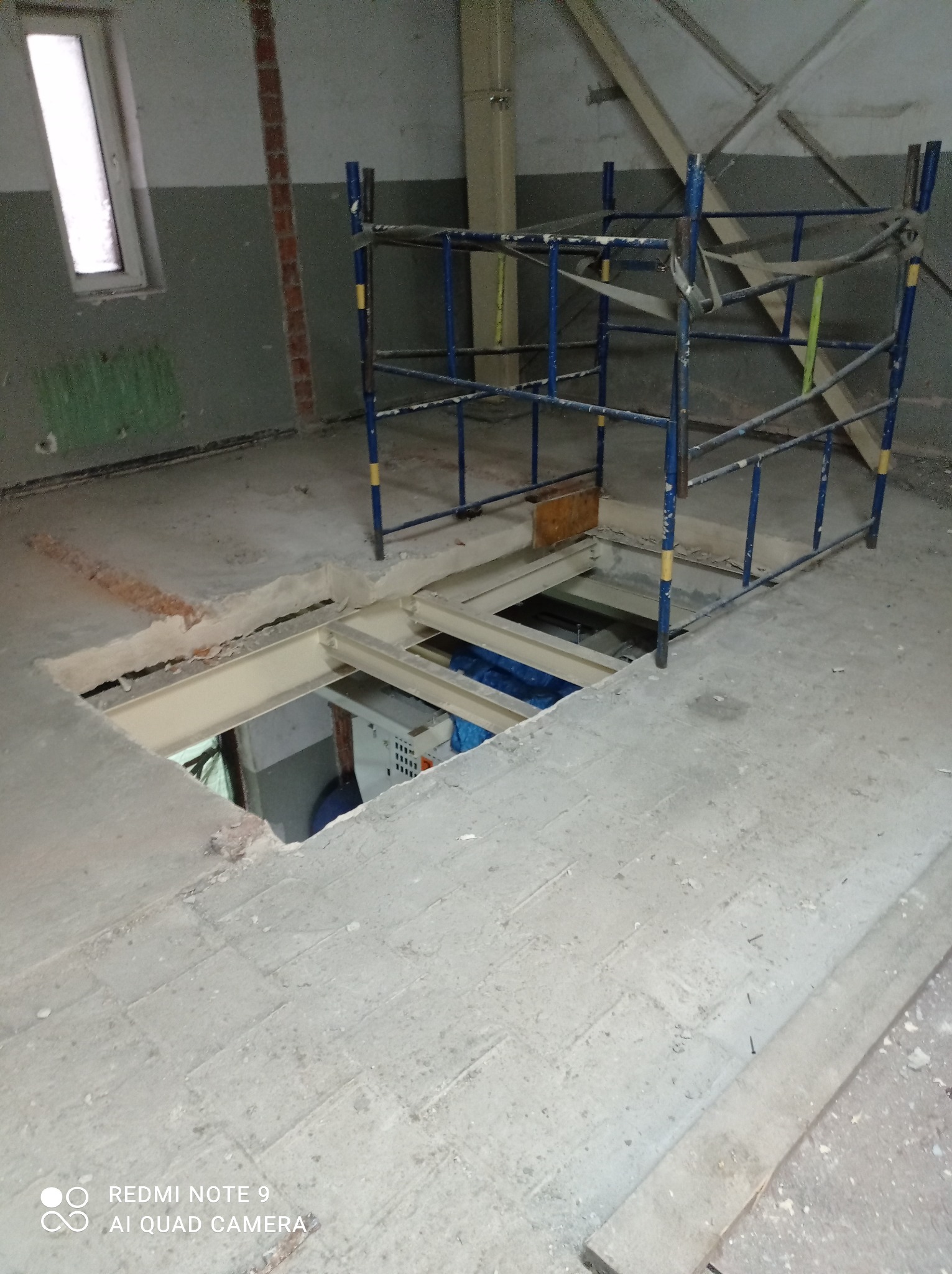 Otwór w podłodze w trakcie remontu, zabezpieczony rusztowaniem, widoczne elementy instalacji w przestrzeni pod podłogą.