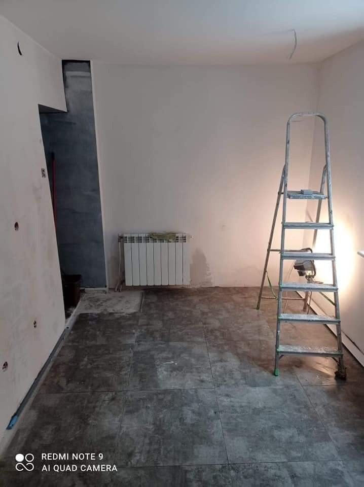 Pokój w trakcie remontu z położoną szarą podłogą, białe ściany, grzejnik i aluminiowa drabina