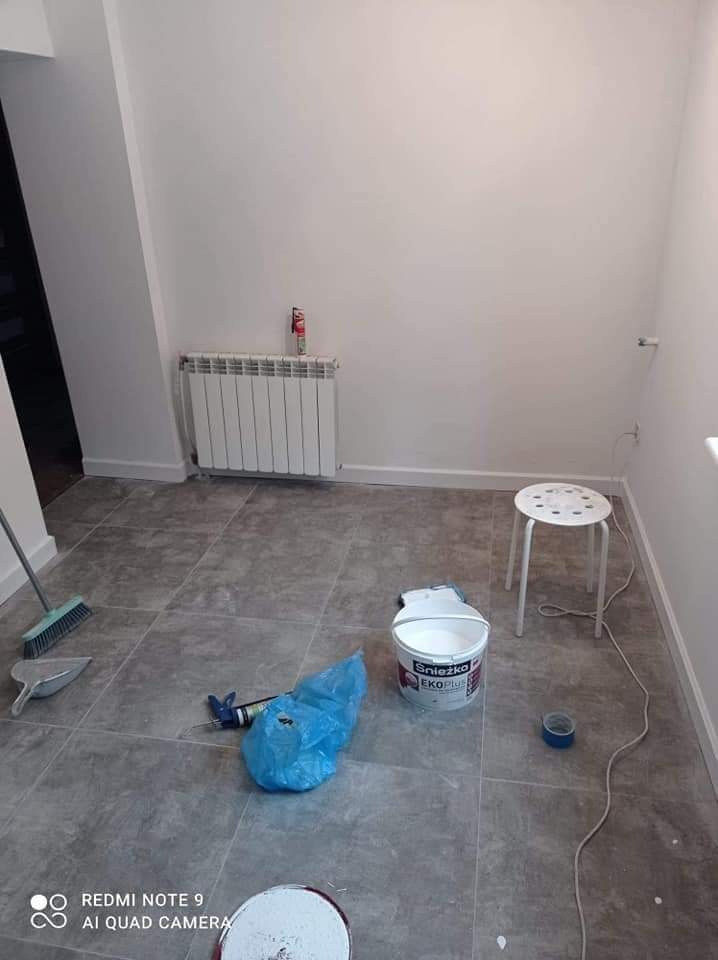 Przygotowane pomieszczenie do malowania ścian: wiadro z farbą Śnieżka Eko Plus, pędzel, szufelka, taboret i grzejnik.
