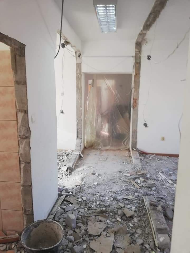 Wnętrze w trakcie demontażu: gruz na podłodze, odsłonięte kable, folia ochronna na drzwiach, widoczne fragmenty płytek.