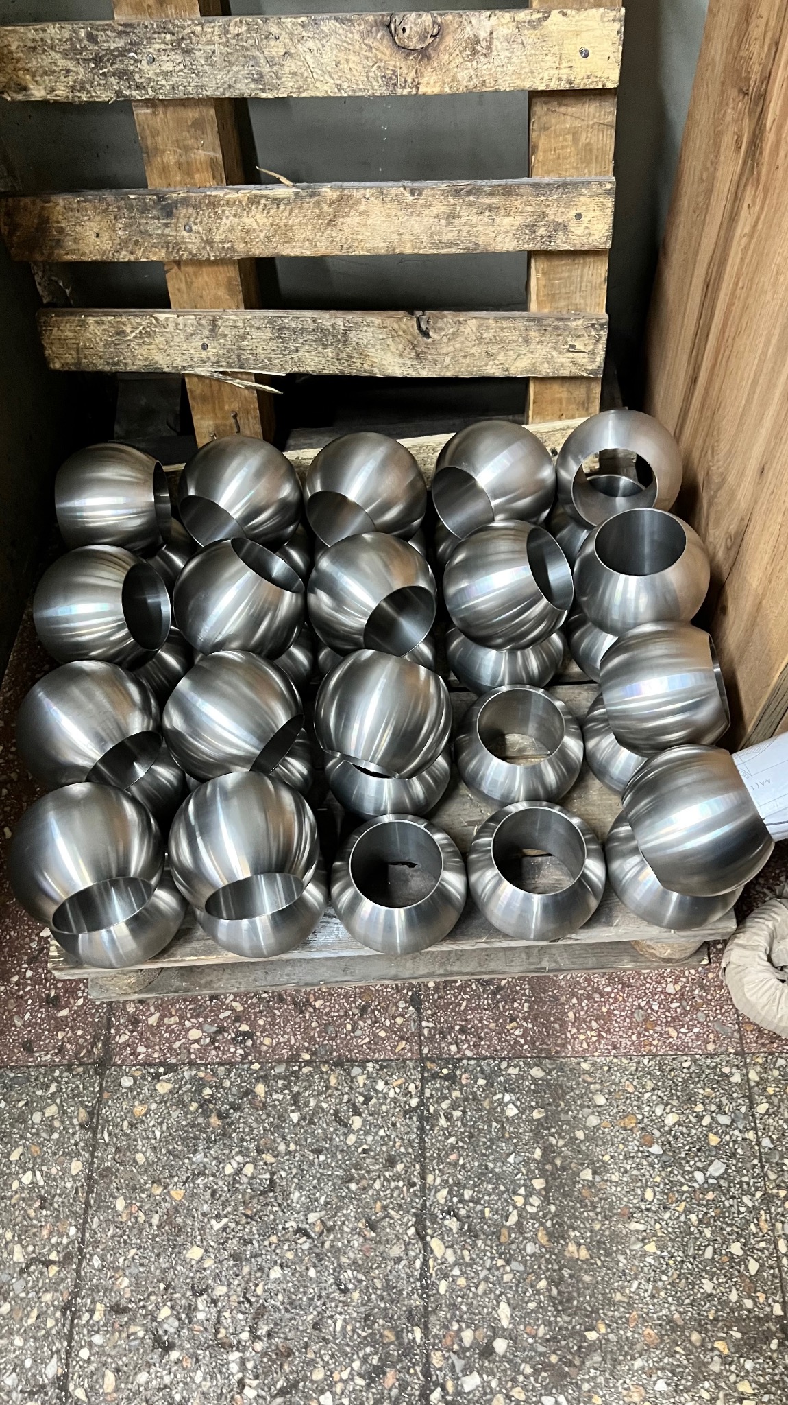 Stalowe półkule z otworem, ułożone warstwami na drewnianej palecie w warsztacie.