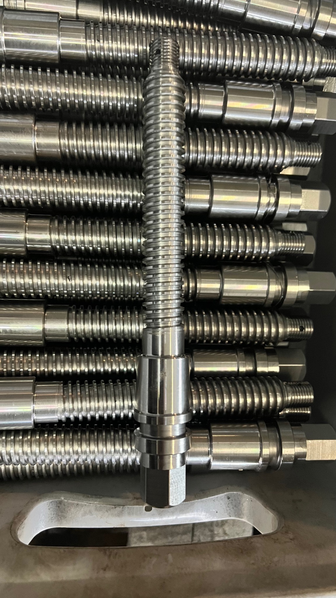 Szereg ułożonych, precyzyjnie obrobionych, metalowych elementów z gwintem, jeden element ustawiony pionowo na pierwszym planie.