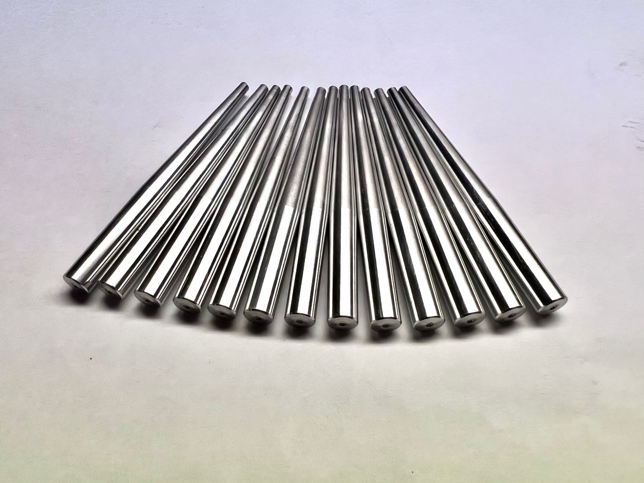 Rząd polerowanych, metalowych prętów z wgłębieniami na końcach, ułożonych wachlarzowo na białym tle, ukazujących precyzję obróbki.