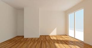 Puste, jasne pomieszczenie z parkietem i dużym oknem przesuwnym; wpadające promienie słoneczne podkreślają strukturę drewna.