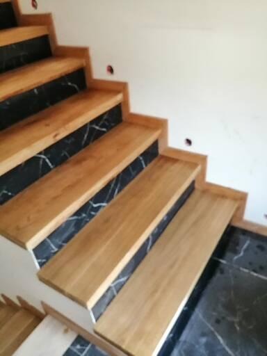 Schody z drewnianymi stopniami i okładziną z czarnego marmuru z białymi żyłami, widok z dołu na górę.