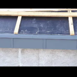 Fundament zabezpieczony czarną izolacją, z widoczną konstrukcją drewnianą i szarą obudową, przygotowany do dalszych prac.