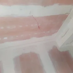 Ściany i sufit w trakcie szpachlowania, widoczne ślady po łatach gipsowych, wystający przewód elektryczny i puszka instalacyjna.