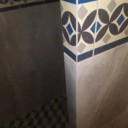 Wykończona łazienka w Żywcu z mozaikową podłogą i dekoracyjną listwą ceramiczną z motywem geometrycznym, szare płytki na ścianach.