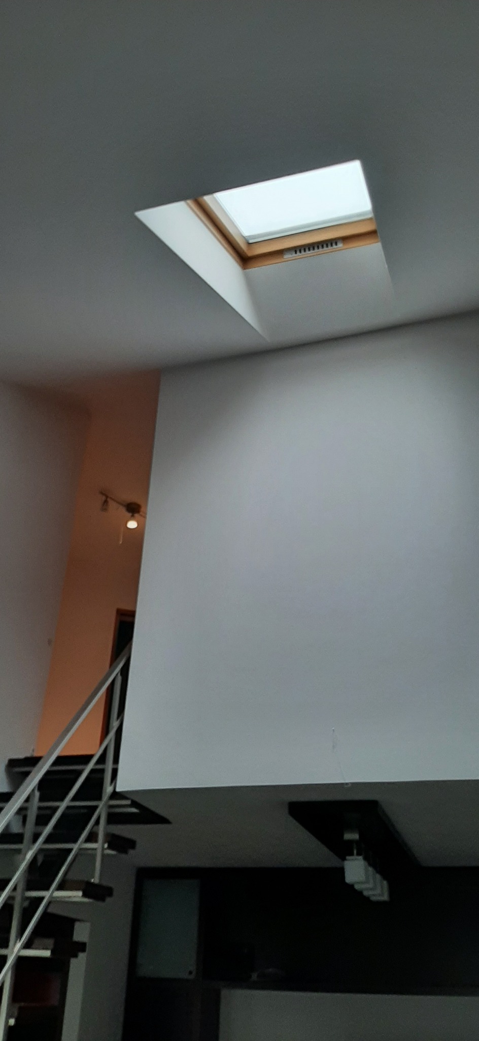 Wnętrze domu w Krakowie z białymi ścianami, schodami ze srebrną balustradą i oknem dachowym z drewnianą ramą.