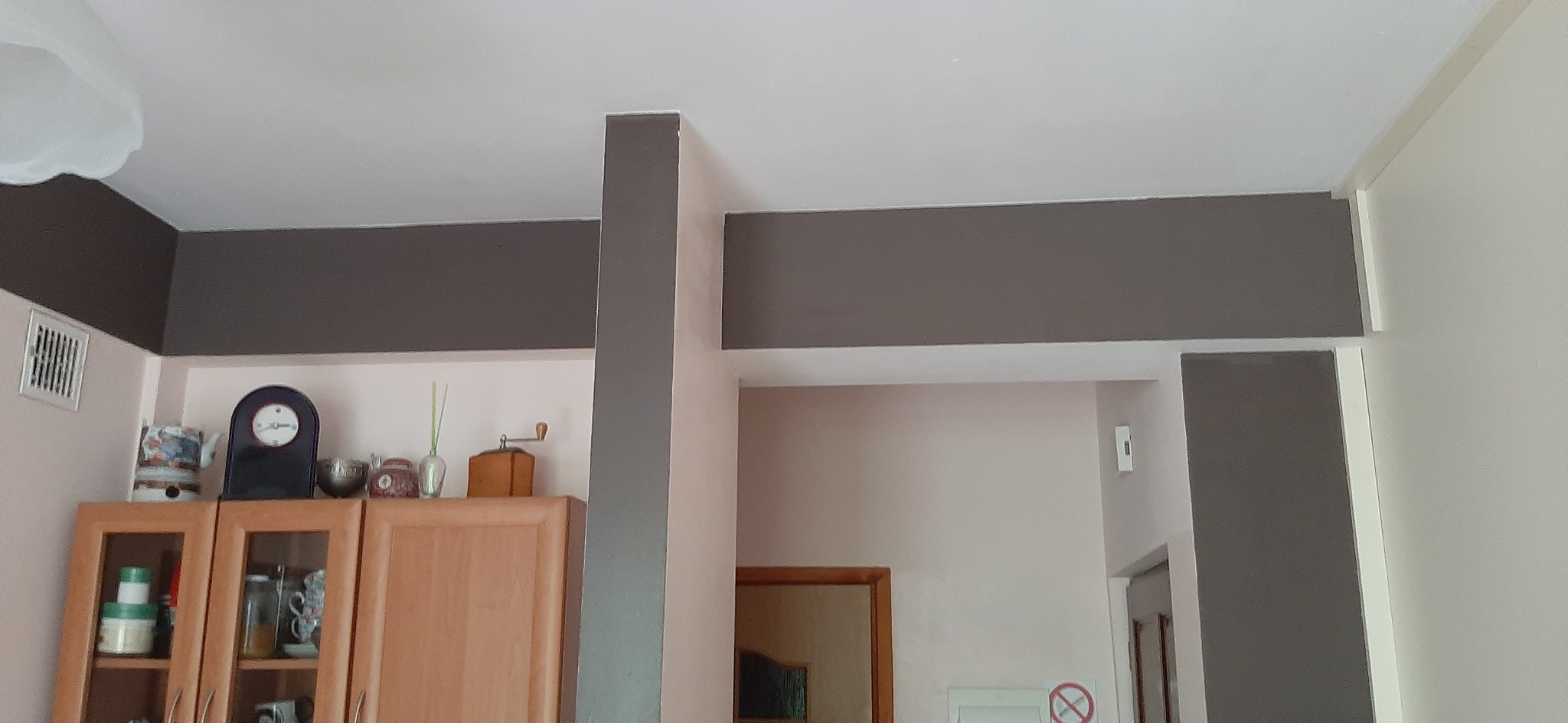 Pomieszczenie po odświeżeniu: szare pasy na ścianach i suficie, widoczna szafka kuchenna z dekoracjami.