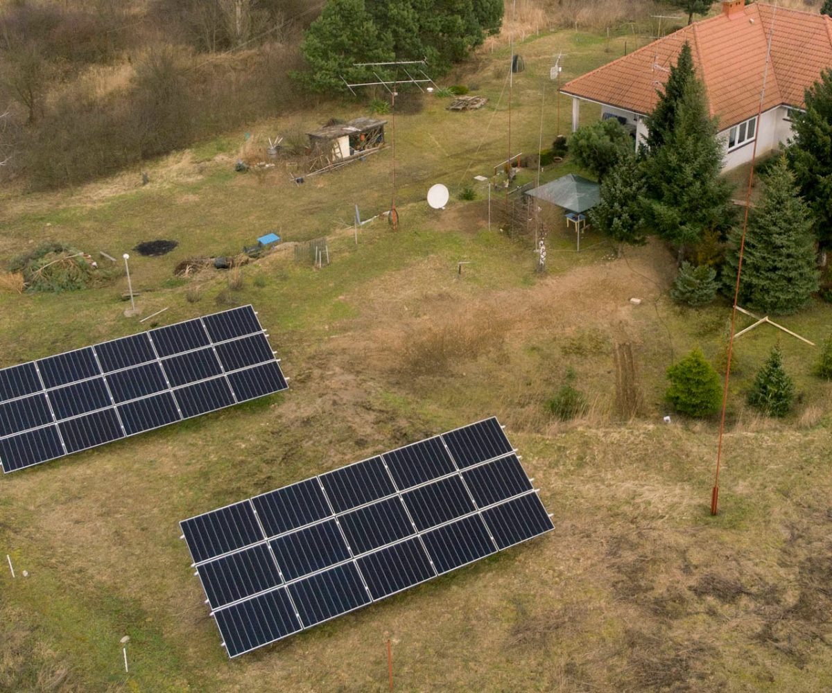 Dwa panele słoneczne na trawiastym terenie przed domem jednorodzinnym, widok z góry.