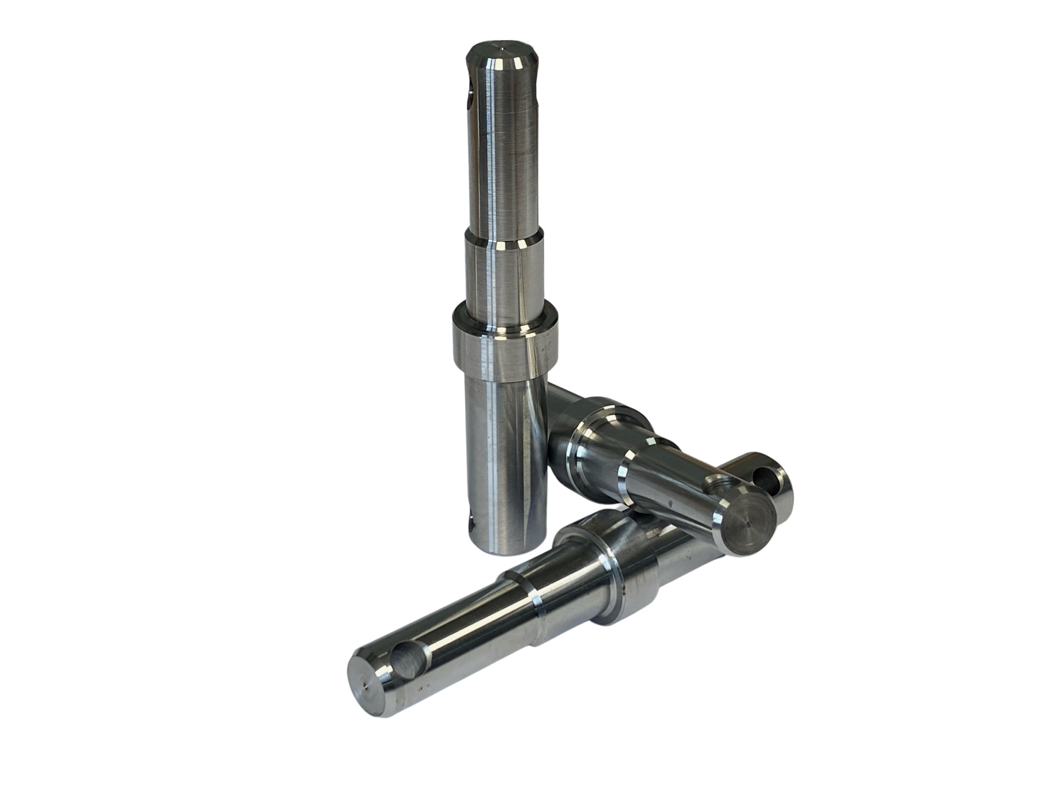 Trzy precyzyjnie obrobione, metalowe trzpienie z otworami, ułożone na białym tle w studyjnym oświetleniu, prezentujące detale obróbki CNC.