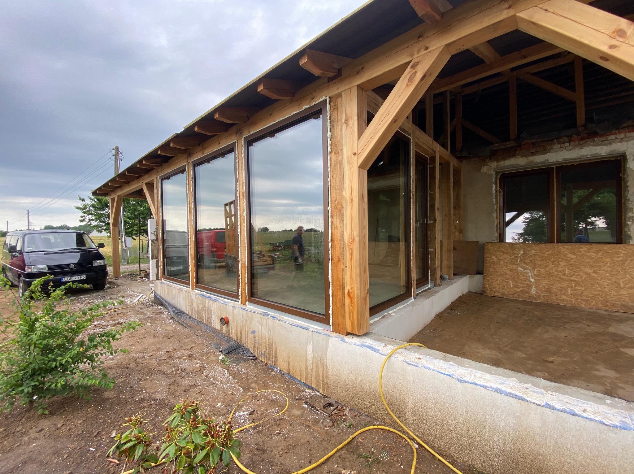 Montaż dużych okien w drewnianej konstrukcji budynku w trakcie budowy, widoczne pianowanie i surowy stan wykończenia.