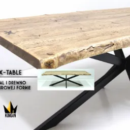 Stół z blatem z jasnego drewna o nieregularnych krawędziach, wsparty na czarnej, metalowej podstawie w kształcie litery X; widoczne słoje drewna i niewielkie wstawki w kształcie krzyżyków; w tle...