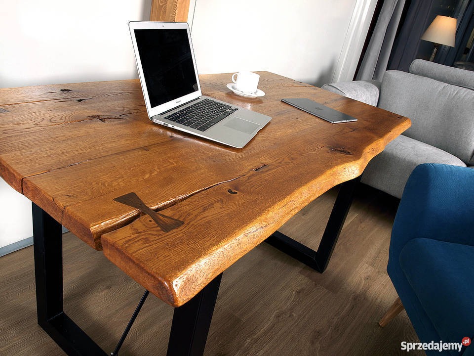 Stół z blatem z litego drewna dębowego z naturalną krawędzią, wykończony na wysoki połysk, z czarnymi metalowymi nogami w kształcie litery V, wzmocniony motylkiem z ciemniejszego drewna, na blacie...