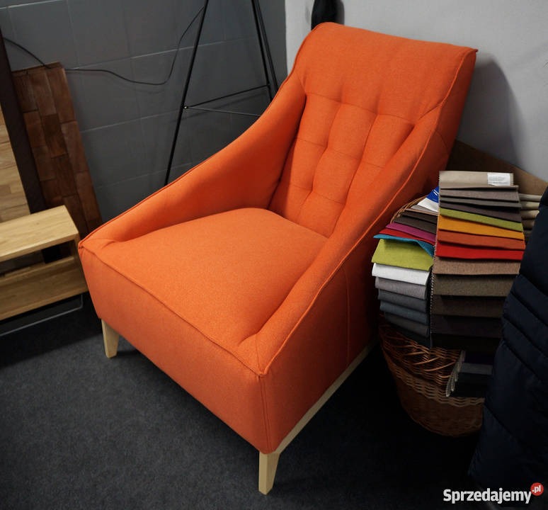 Pomarańczowy fotel tapicerowany z wysokim oparciem i pikowaniem, prezentowany obok próbek materiałów w koszyku.