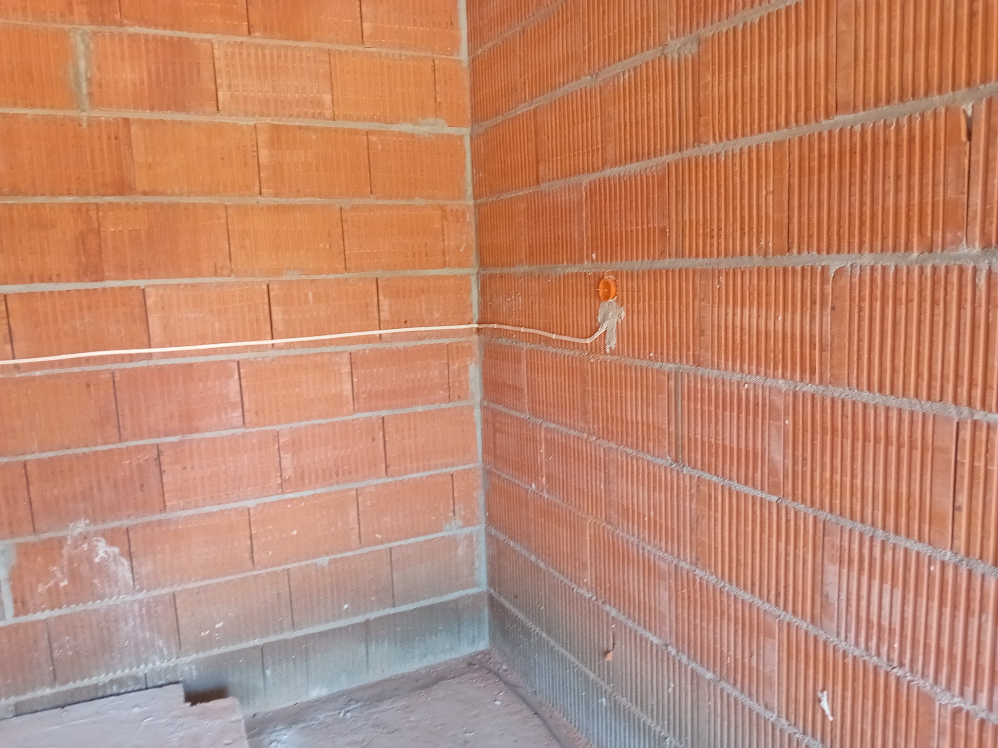 Wewnętrzny róg budynku z cegły ceramicznej z poprowadzoną instalacją elektryczną w peszlu i puszką pod gniazdko.