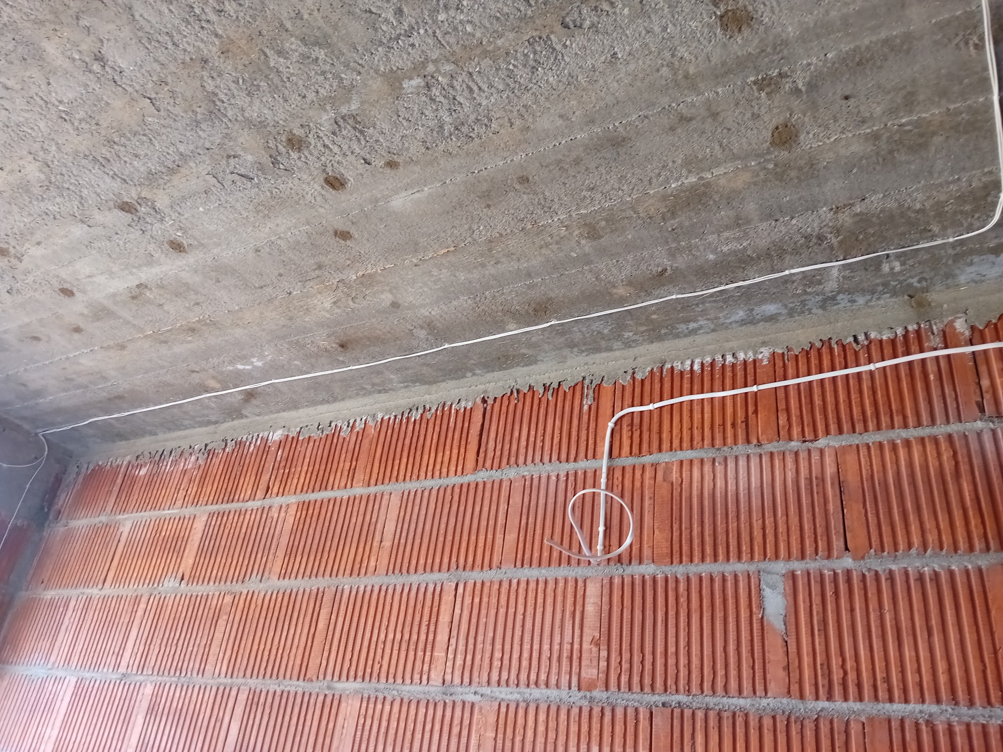 Surowy betonowy sufit i ściana z czerwonej cegły z widocznymi przewodami elektrycznymi, etap prac w nowym budynku.