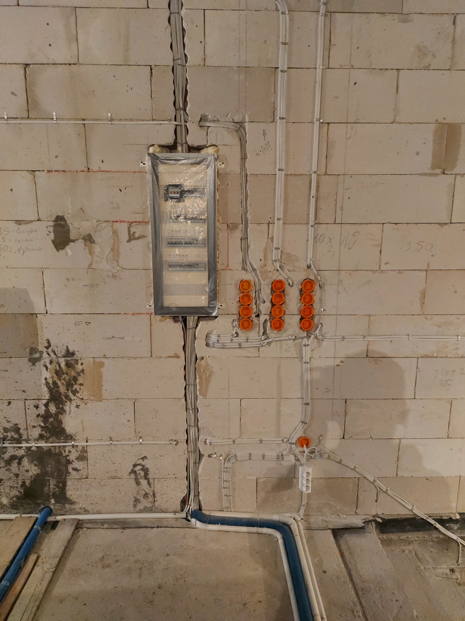 Rozdzielnia elektryczna zabezpieczona folią na ścianie z betonu komórkowego, widoczne kable w peszlach i puszkach instalacyjnych, instalacja w trakcie montażu.