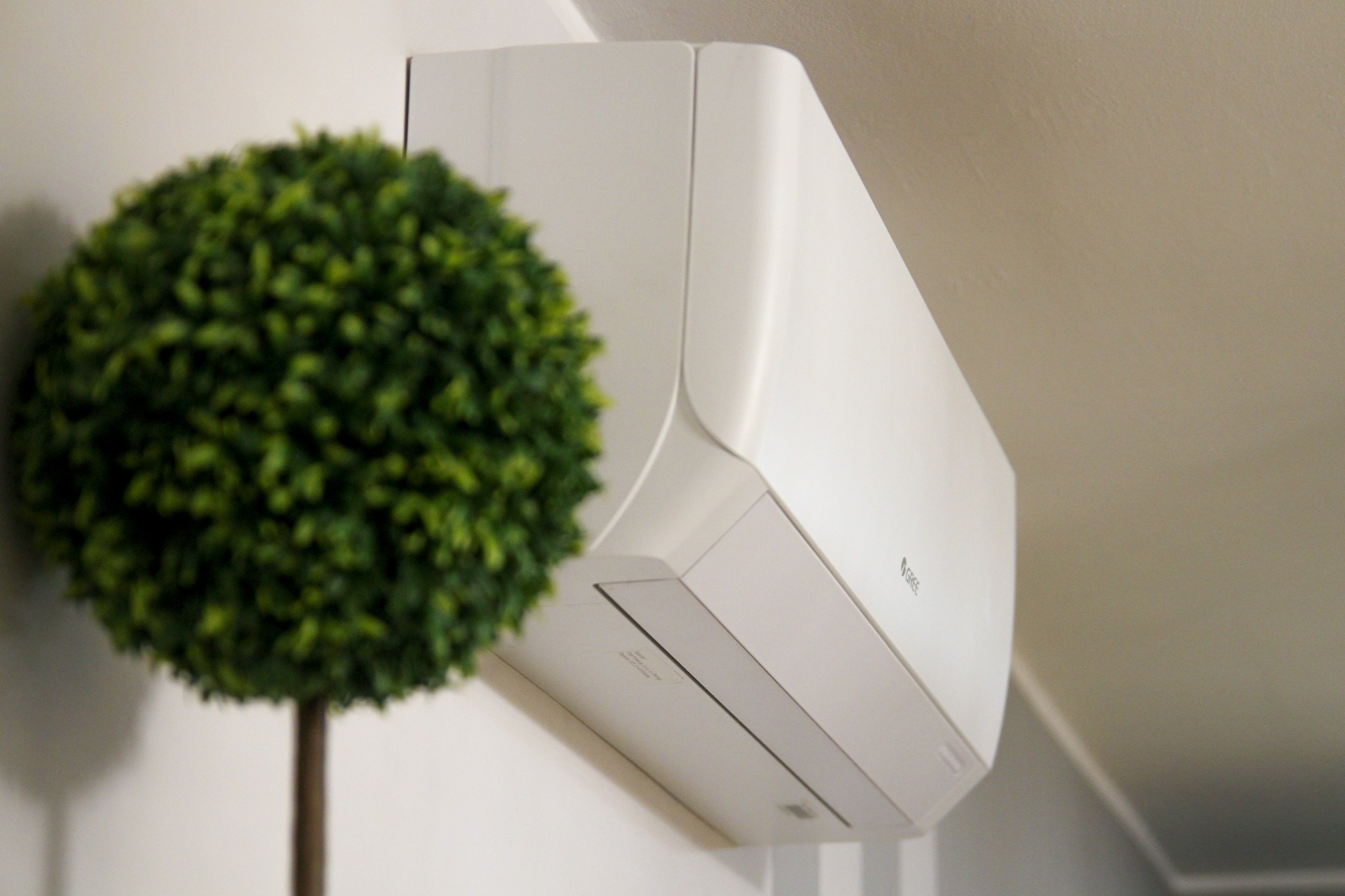 Biała klimatyzacja marki Gree zamontowana na ścianie, obok dekoracyjna zielona kula z roślin.
