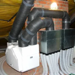 Kompletny system rekuperacji z odzyskiem ciepła w trakcie instalacji na poddaszu, widoczne izolowane rury wentylacyjne, centrala rekuperacyjna, rozdzielacze i przewody wentylacyjne, z żółtą folią...