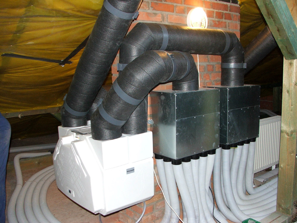 Kompletny system rekuperacji z odzyskiem ciepła w trakcie instalacji na poddaszu, widoczne izolowane rury wentylacyjne, centrala rekuperacyjna, rozdzielacze i przewody wentylacyjne, z żółtą folią...