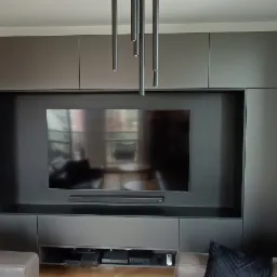 Ciemnoszara zabudowa meblowa na ścianie z wnęką na telewizor i sprzęt audio-wideo, minimalistyczne lampy wiszące, widok z salonu.