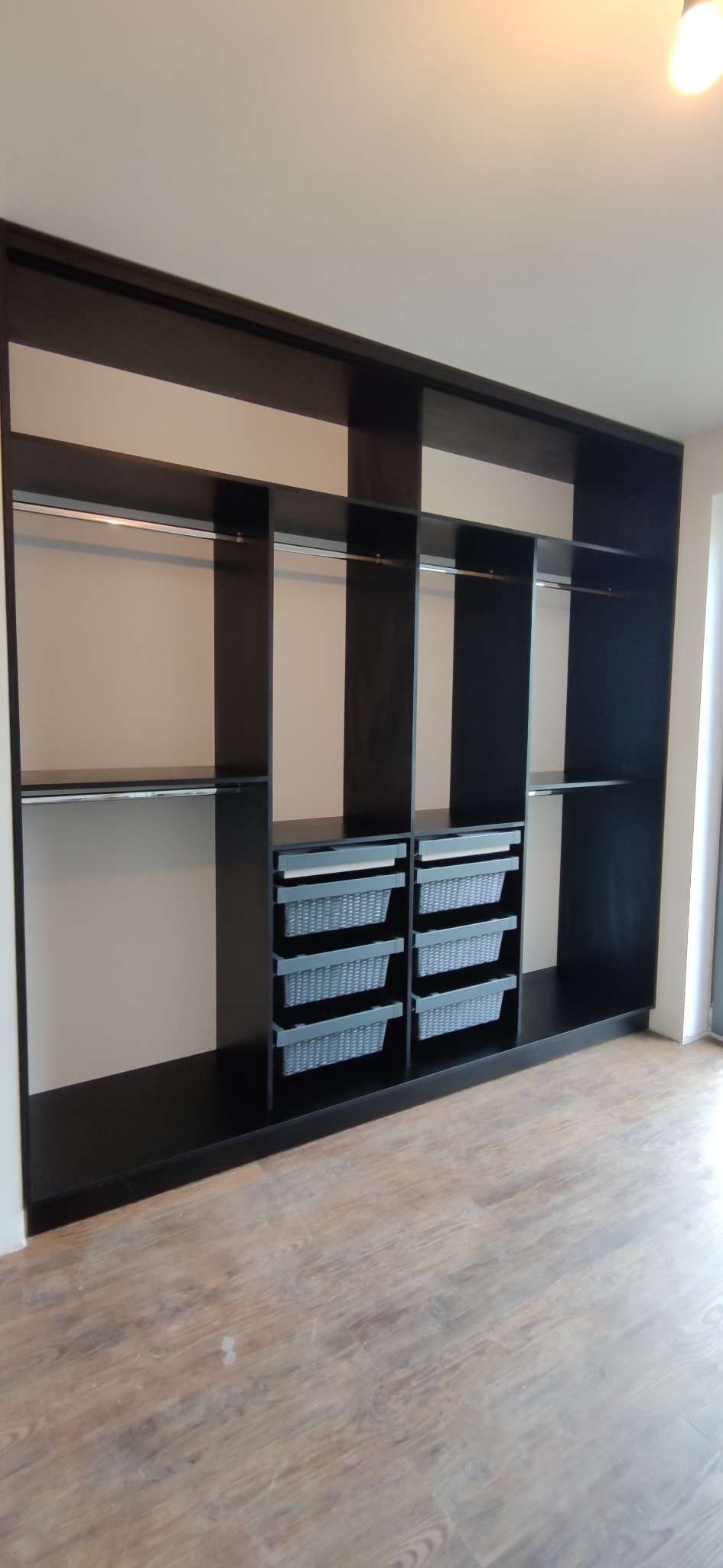 Czarna szafa wnękowa z szufladami i drążkami na ubrania, wykonana na wymiar w Elblągu, na podłodze panele imitujące drewno.