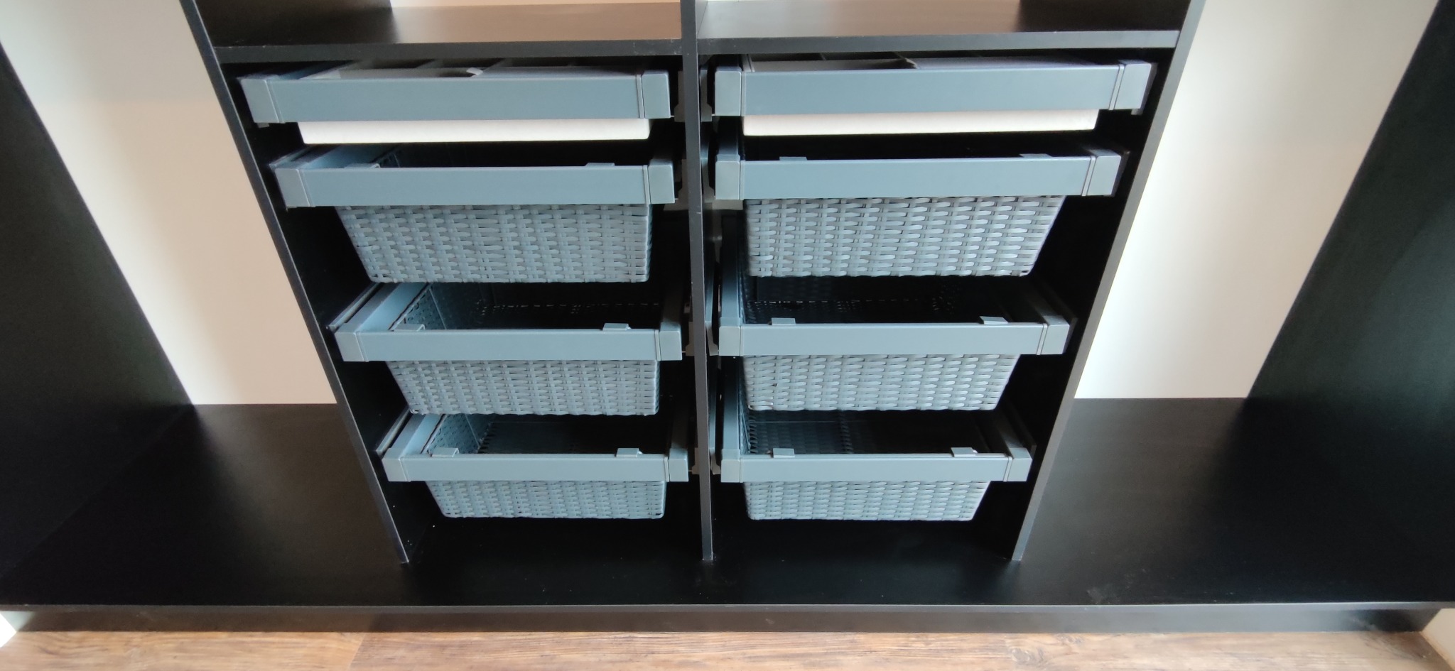 Wnętrze szafy z wysuwanymi koszami z tworzywa sztucznego imitującego rattan, szare kosze na szynach w czarnej obudowie.