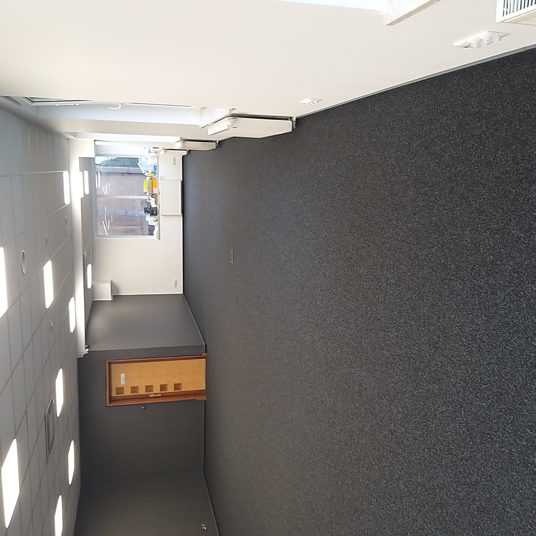 Wnętrze biura po malowaniu ścian na szaro z widoczną tablicą ogłoszeń i oknem na końcu korytarza.