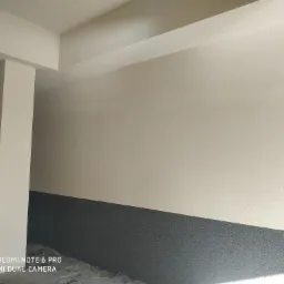 Świeżo pomalowane wnętrze budynku z dwukolorową ścianą (beżowa g&oacute;ra i szary d&oacute;ł) oraz kolumną. Widoczna faktura tynku.