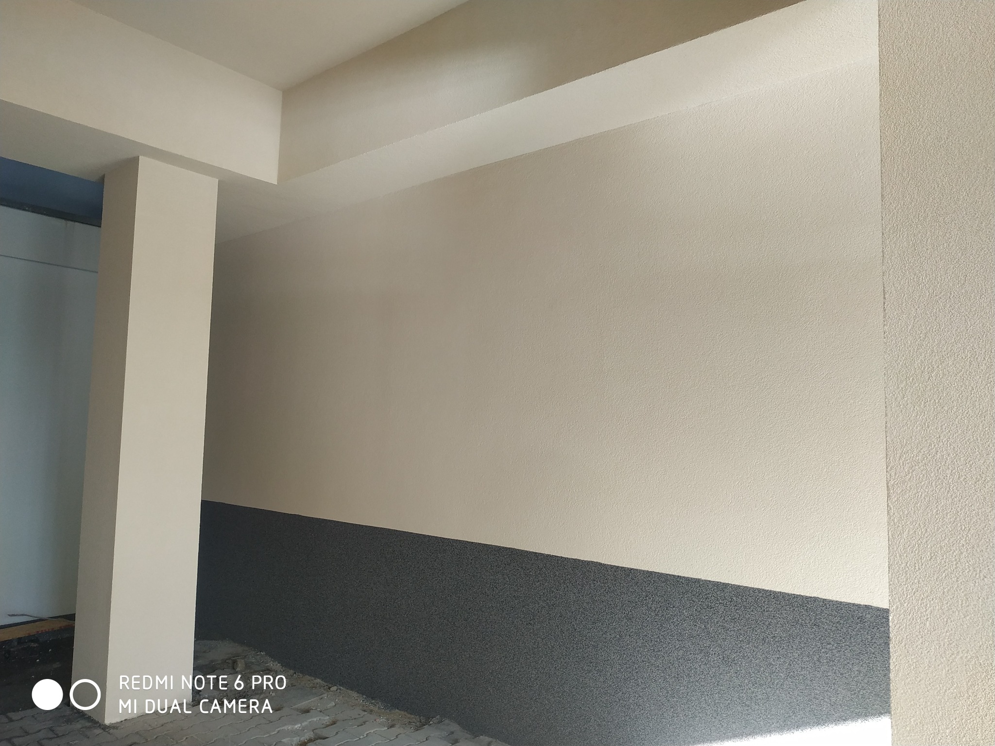 Świeżo pomalowane wnętrze budynku z dwukolorową ścianą (beżowa góra i szary dół) oraz kolumną. Widoczna faktura tynku.