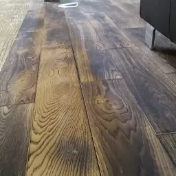 Podłoga z ciemnego drewna w trakcie renowacji w Krakowie, widoczne niedoskonałości i ślady po cyklinowaniu, w tle narzędzia i meble.