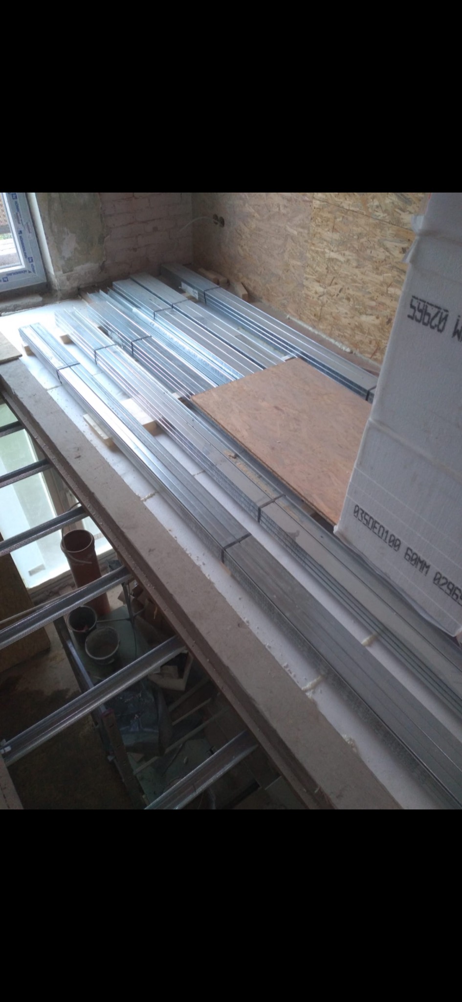 Przygotowane profile metalowe do montażu sufitu podwieszanego, płyta OSB oraz puszka z pianką montażową na podłodze w trakcie remontu.