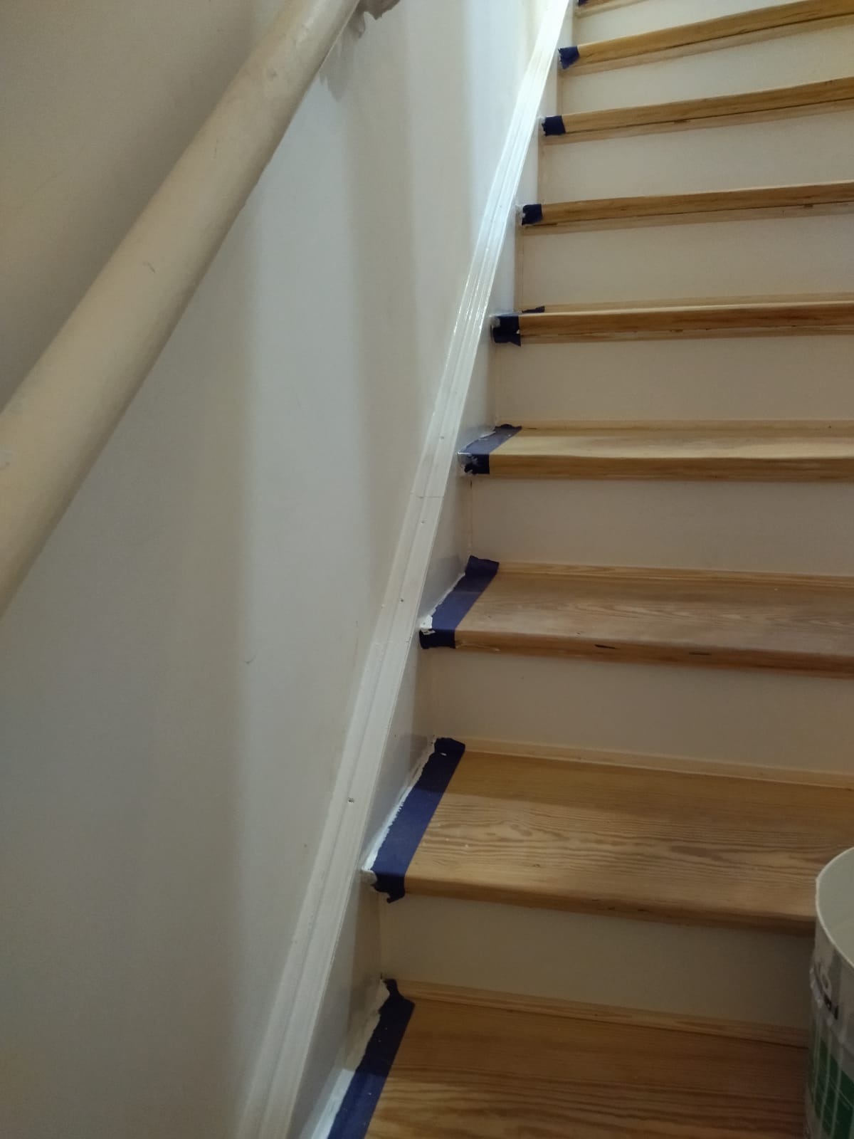 Schody drewniane zabezpieczone taśmą malarską przed malowaniem ściany i listwy przypodłogowej na biało.