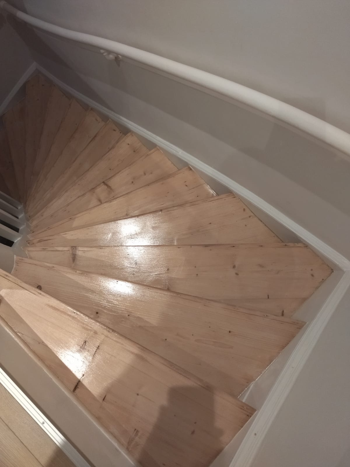 Spiralne drewniane schody po renowacji, świeżo polakierowane, widok z góry, jasne drewno.