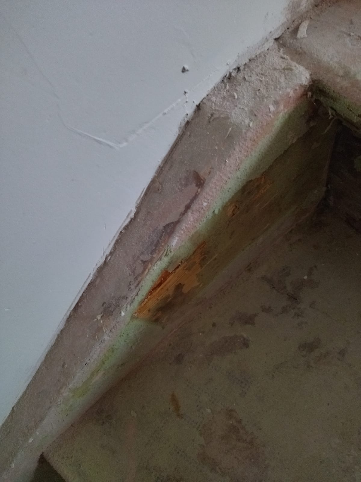 Narożnik ściany i podłogi w trakcie remontu, widoczne ślady starej farby i wilgoci, przygotowanie do dalszych prac wykończeniowych.