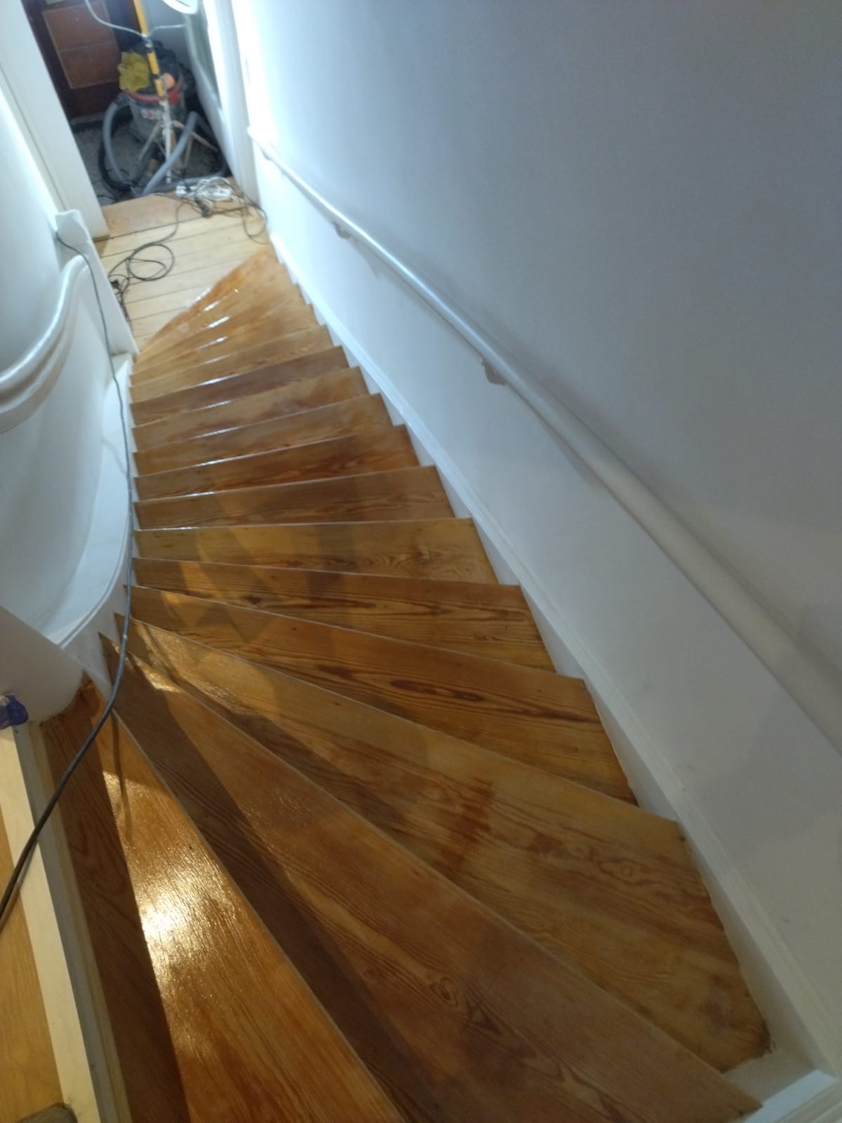 Drewniane schody po lakierowaniu, widoczny połysk lakieru i odnowiona poręcz, na podłodze w tle stoi odkurzacz przemysłowy.