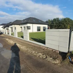 Nowoczesny dom jednorodzinny z szarej kostki ogrodzeniowej w Brzegu Dolnym, widoczny cień osoby fotografującej.