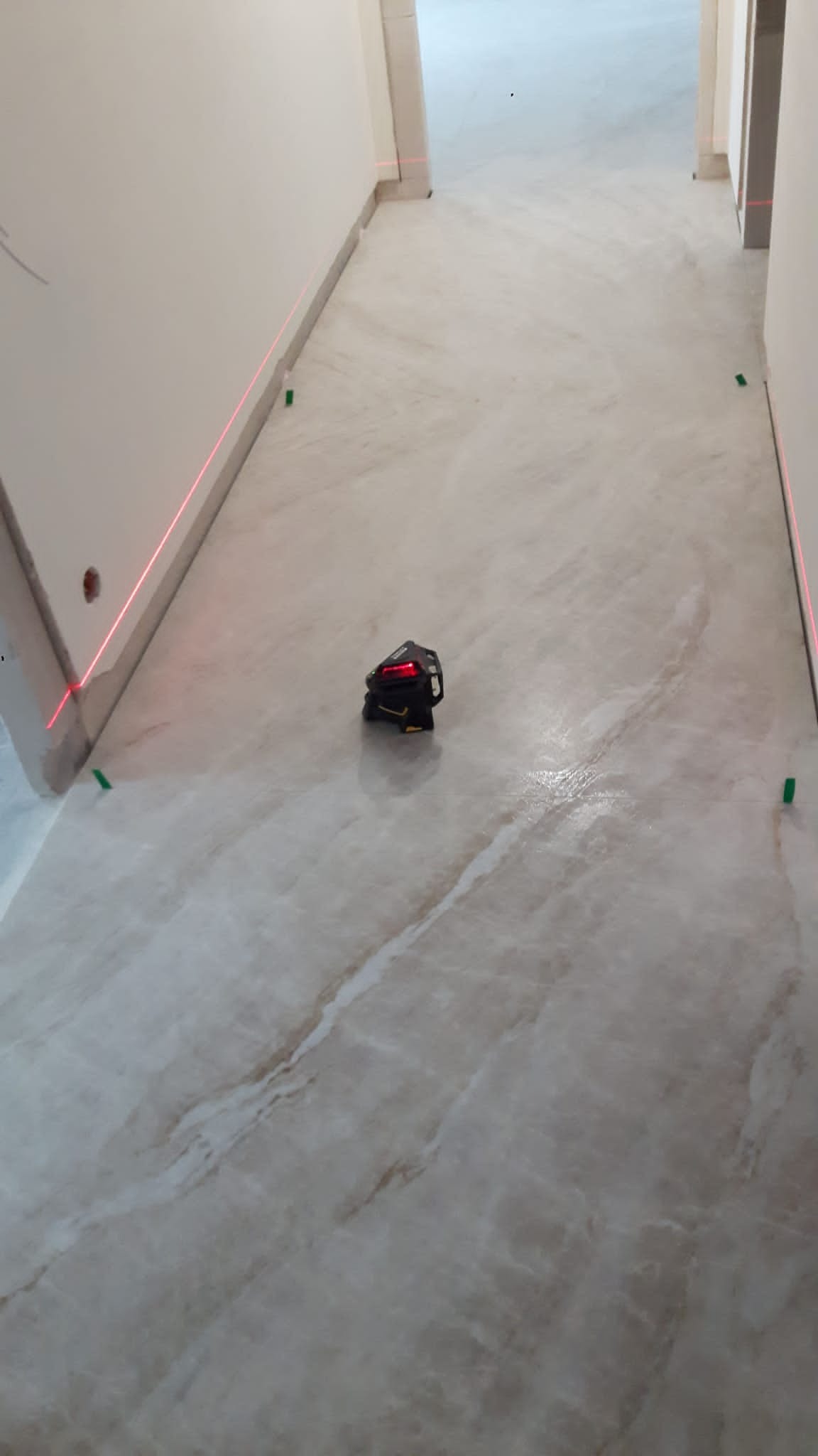 Ułożona marmurowa posadzka w korytarzu, poziomowana laserem, widoczne zielone podkładki dystansowe.