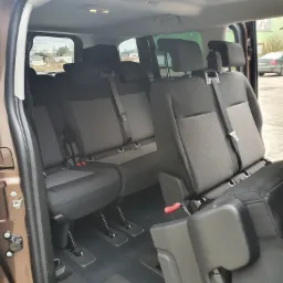 Wnętrze brązowego busa z trzema rzędami foteli w odcieniach szarości i czerni, widoczne mechanizmy regulacji siedzeń.