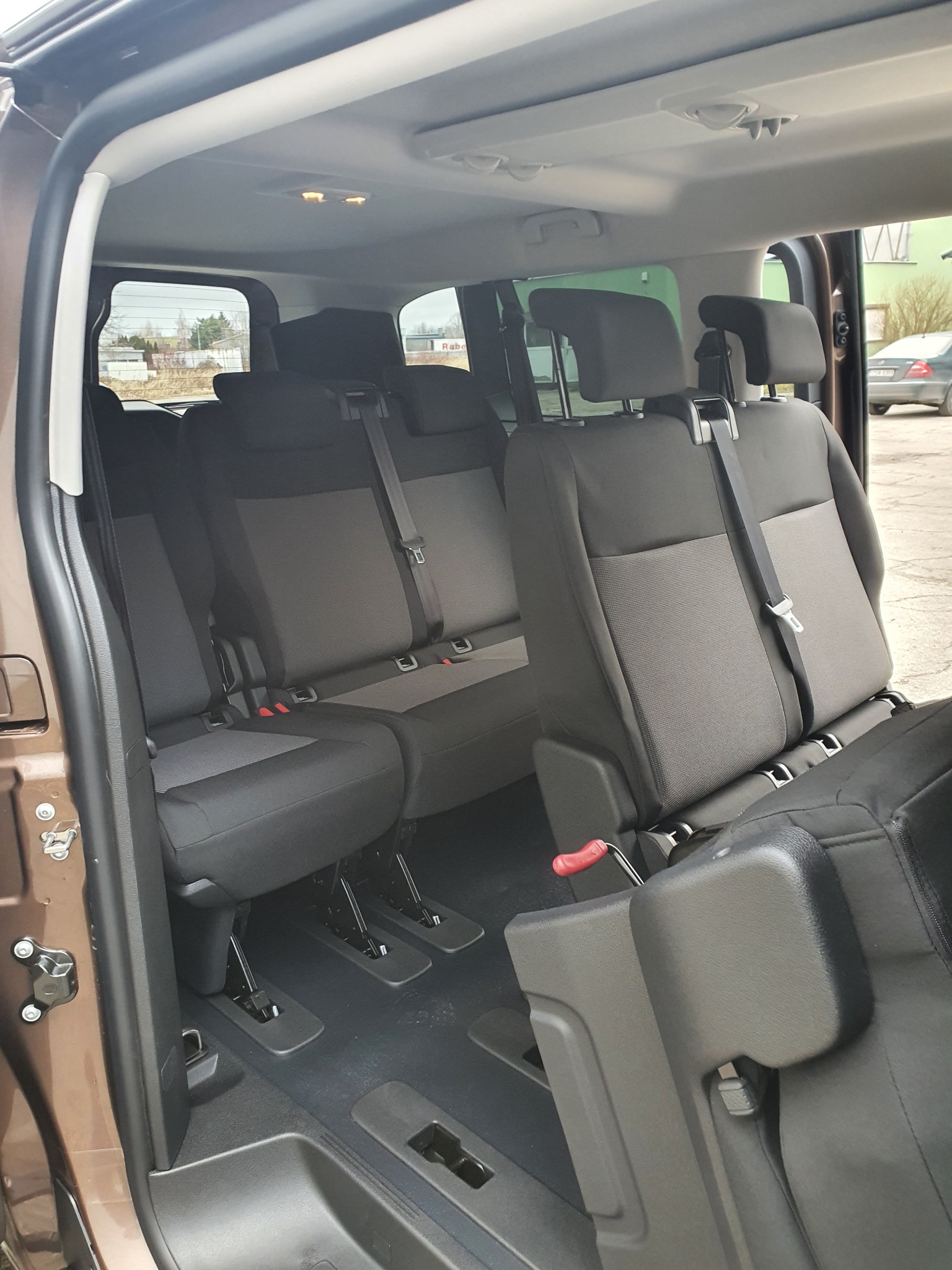 Wnętrze brązowego busa z trzema rzędami foteli w odcieniach szarości i czerni, widoczne mechanizmy regulacji siedzeń.