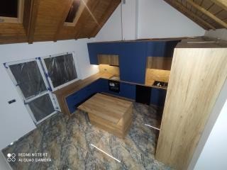 Niebieska zabudowa kuchenna z drewnianymi elementami pod skośnym dachem, widok z góry na wyspę kuchenną i okna zabezpieczone folią.