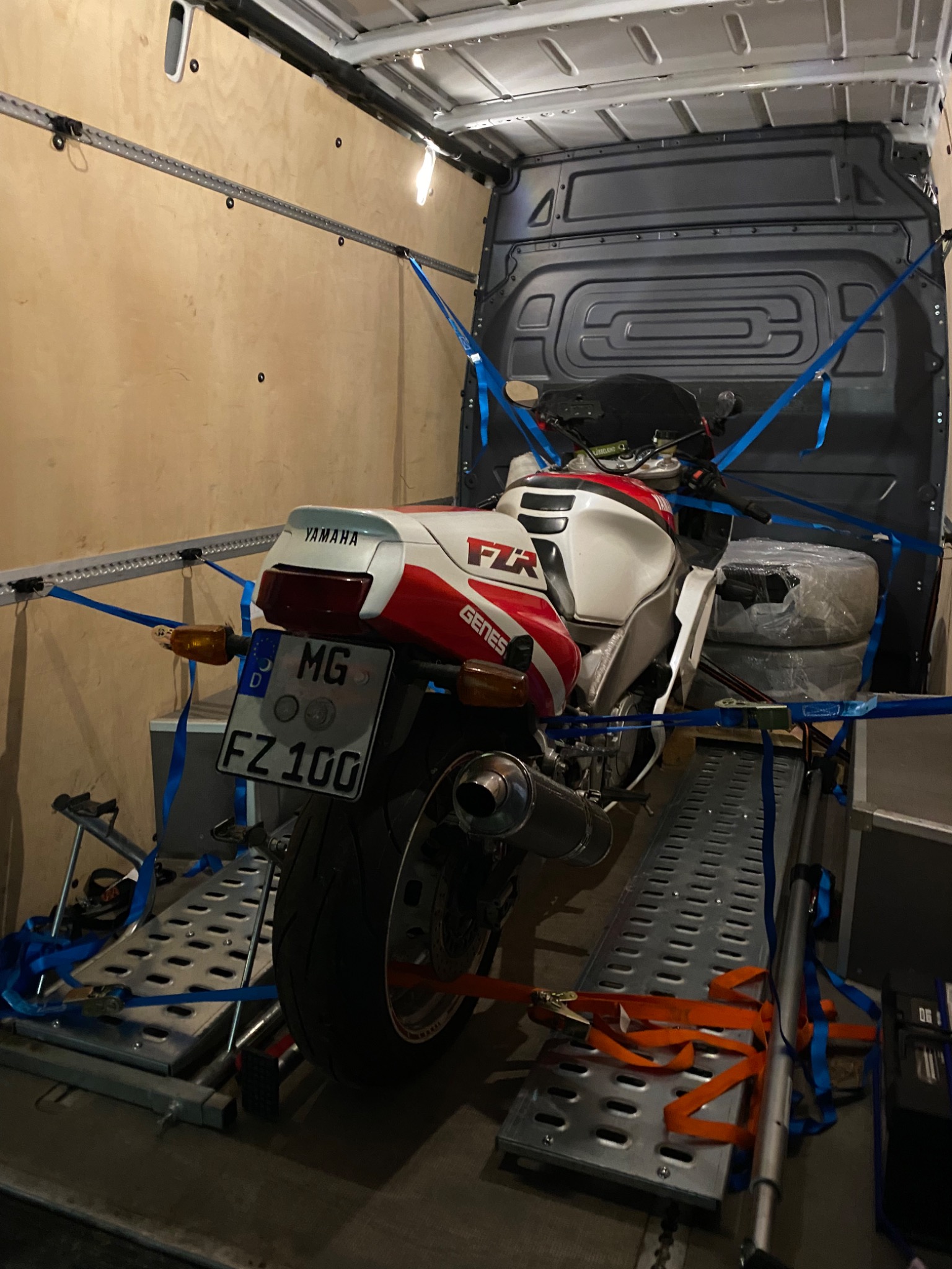 Motocykl Yamaha FZR zabezpieczony pasami transportowymi wewnątrz furgonetki z rampą najazdową, widoczne niemieckie tablice rejestracyjne.