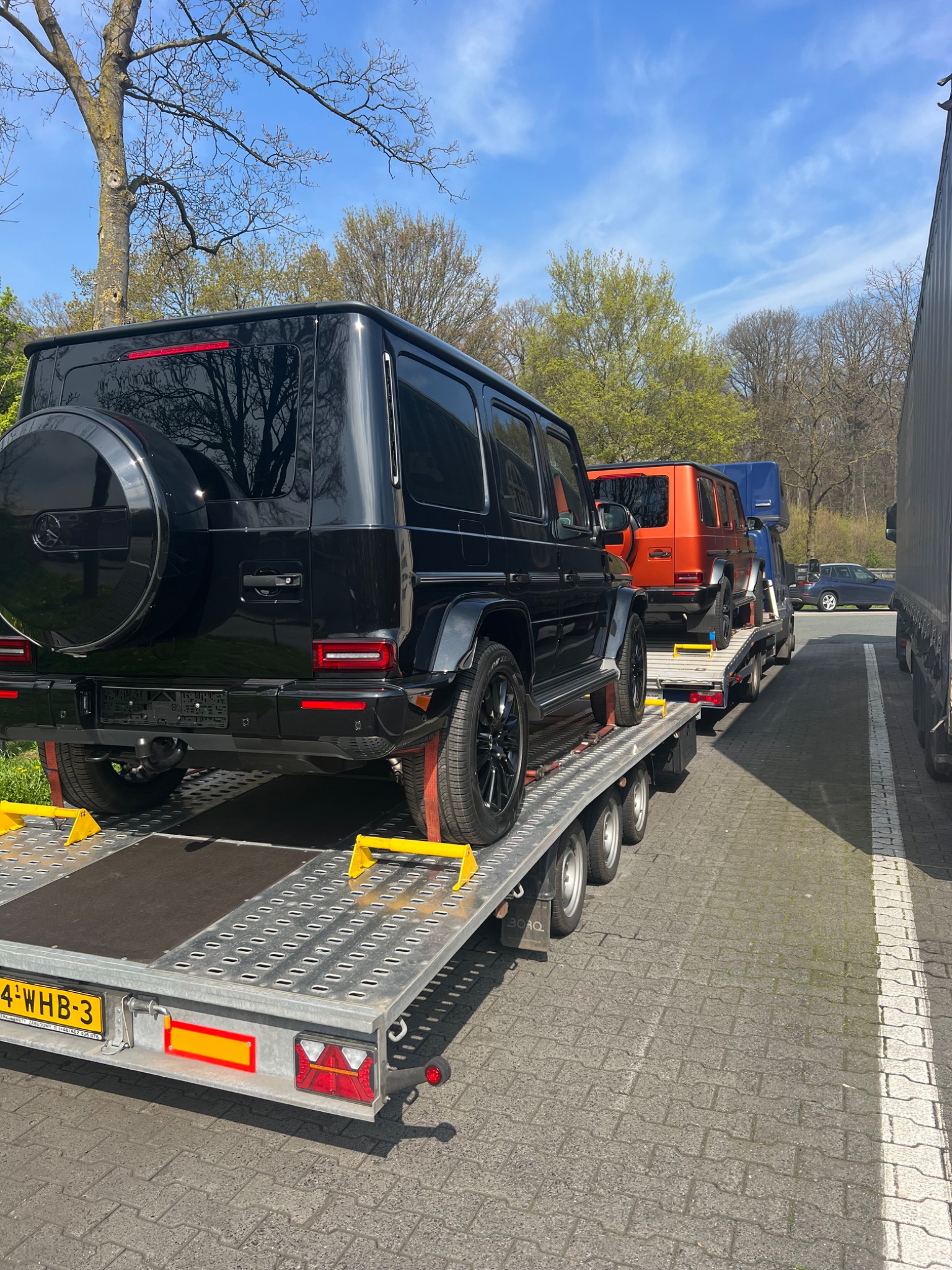 Czarny samochód terenowy na lawecie, widok z tyłu, z widoczną tablicą rejestracyjną i innymi pojazdami na lawecie w tle.