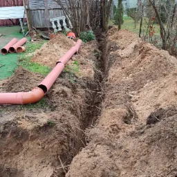 Wykop pod rury kanalizacyjne obok basenu z drabinką; widoczne ułożone rury z tworzywa sztucznego i świeżo usypana ziemia.