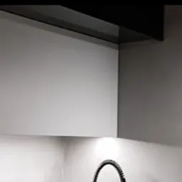 Fragment nowoczesnej kuchni z szarymi, lakierowanymi szafkami wiszącymi i czarnym okapem, oświetlenie punktowe pod szafkami, widoczny fragment baterii kuchennej.